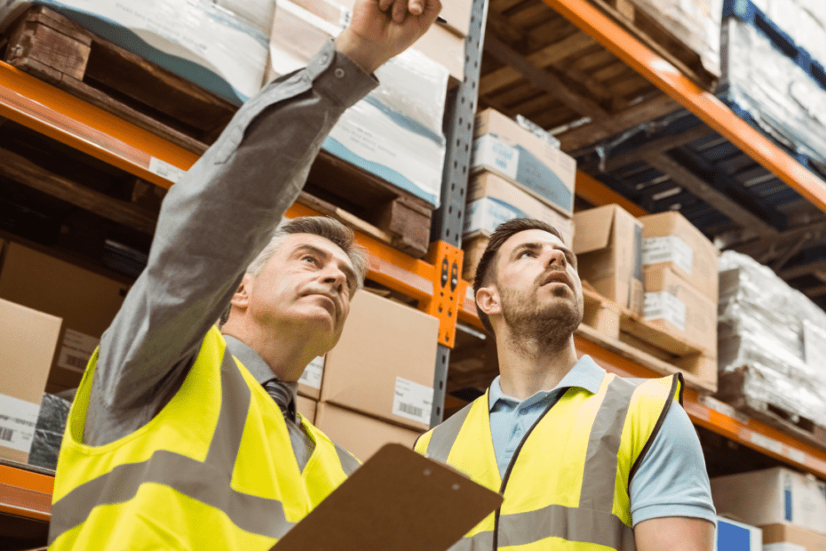 Profissional em almoxarifado com caixas, prateleiras e prancheta ou tablet